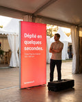 Totem lumineux Pop-Up Express déplié à l'entrée d'un événement, avec sa valise de transport, image générée par IA